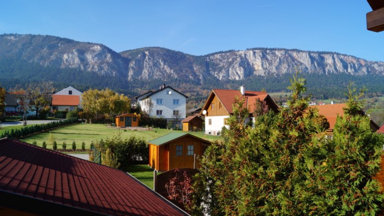 Blick auf H&auml;user mit roten D&auml;chern und Berge im Hintergrund bei klarem Himmel.