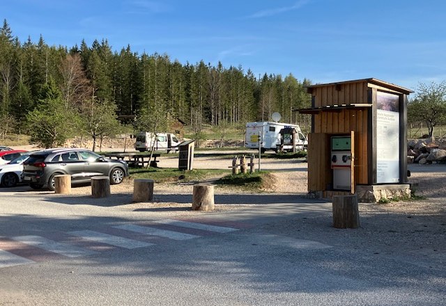 Parkplatz am Naturparkzentrum Hohe Wand mit Autos und Wohnmobilen, umgeben von Wald.