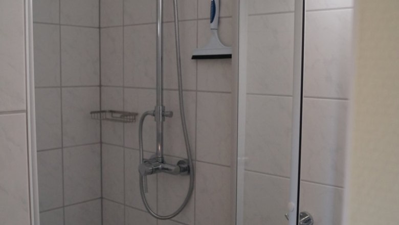 A tiled shower with shower head, shower fitting and squeegee on the wall.
