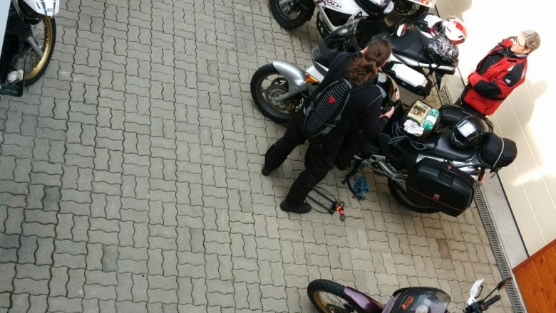 Mehrere Motorr&auml;der und Personen auf einem gepflasterten Platz vor einem Geb&auml;ude.