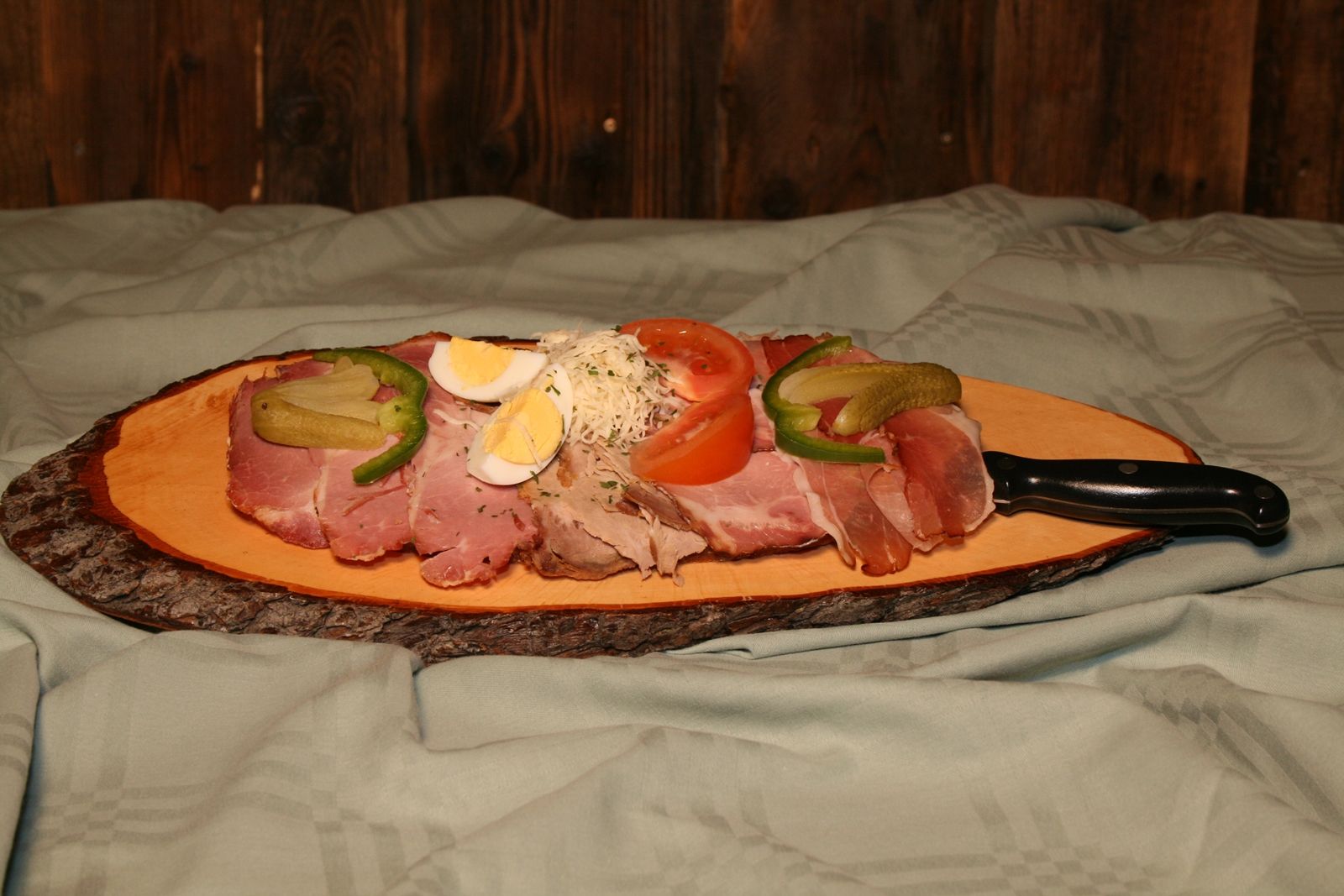 Eine rustikale Jause mit Aufschnitt, Ei, Tomate und Gurke auf einem Holzbrett.