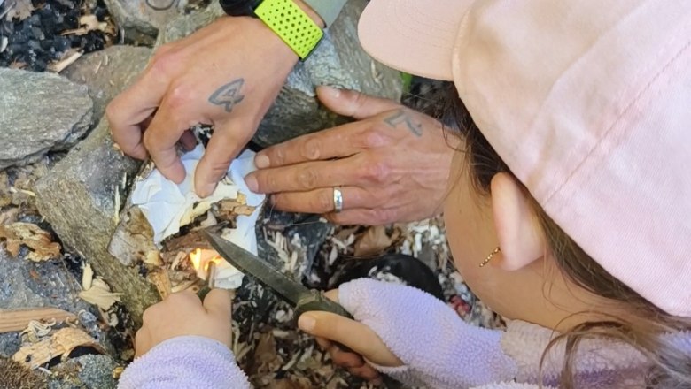 Ein Kind und ein Erwachsener entz&uuml;nden ein Feuer im Freien mit einem Messer und Zunder.