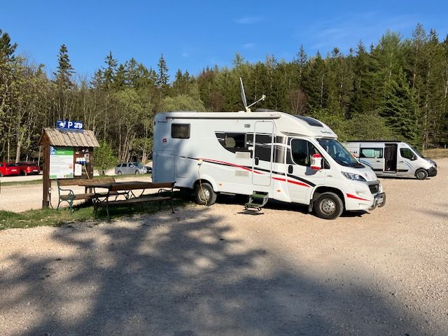 Motorhome in a parking lot in the Hohe Wand Nature Park, surrounded by trees and a blue sky.