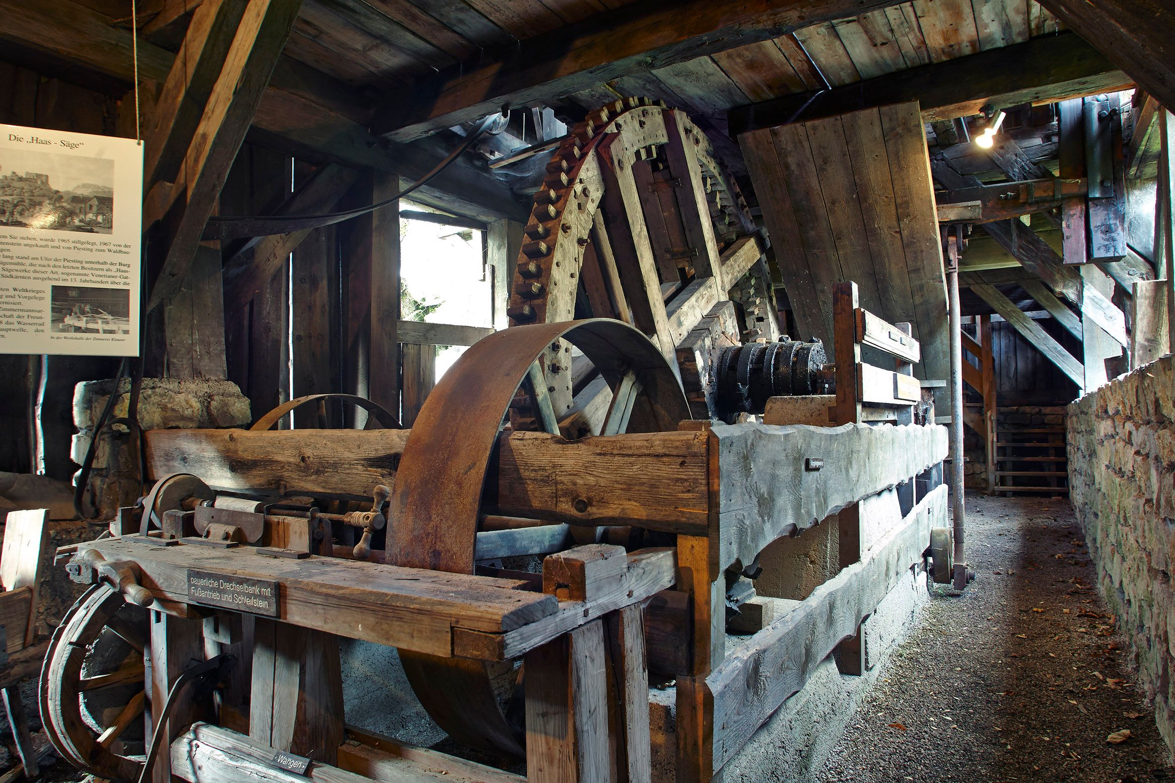Innenansicht eines historischen Sägewerks mit großen Holzzahnrädern und Holzbalken.