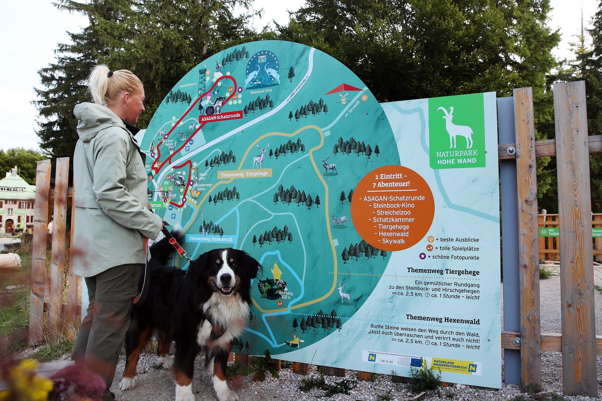 Eine Person steht mit ihrem Hund vor der Übersichtstafel beim Eingang Naturpark Zentrum