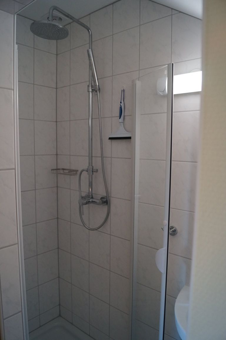 Modern zuhanykabin csempével, zuhanyfejjel és üvegfallal.