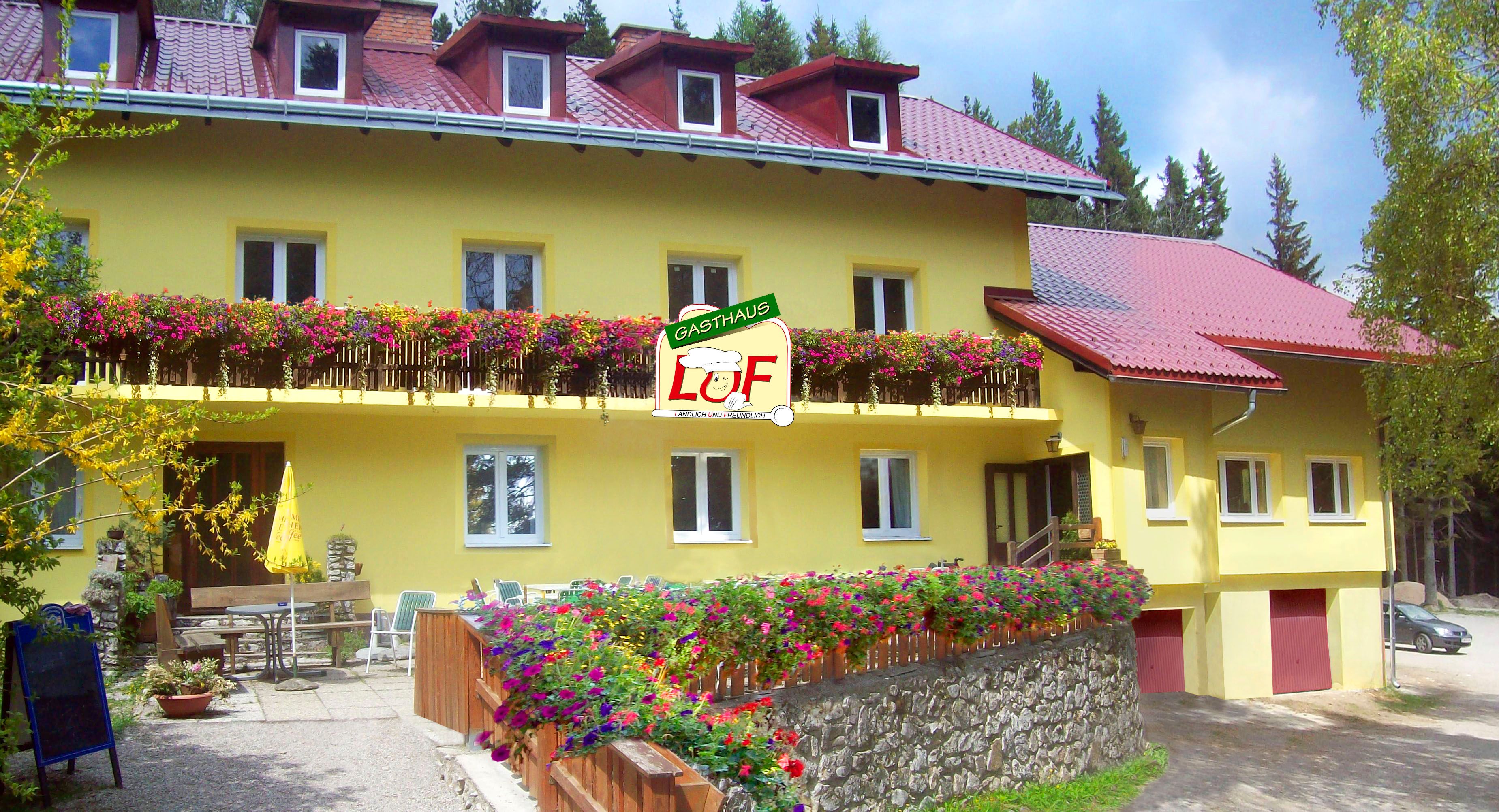 Gelbes Gasthaus mit roten Dächern und blühenden Blumen auf dem Balkon.