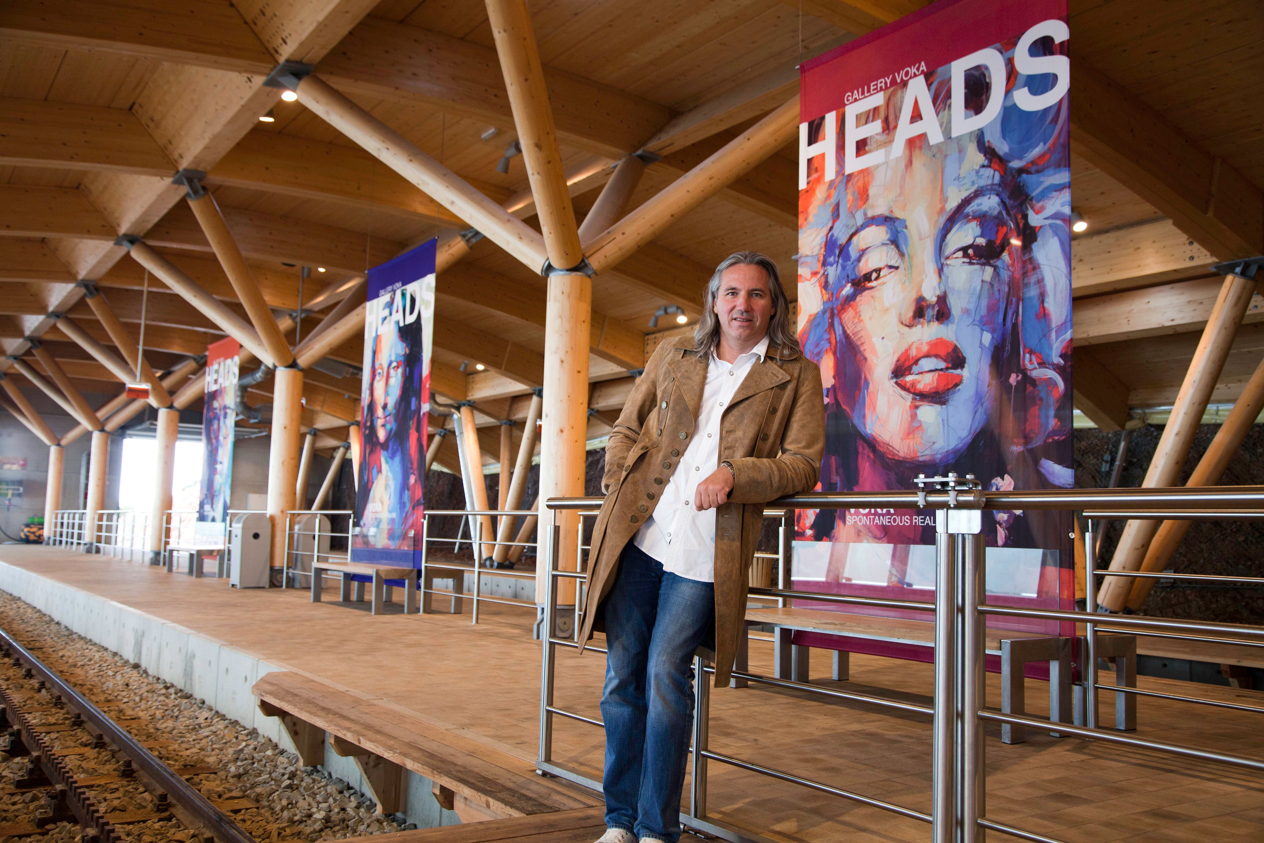 A man stands in a modern train station next to art posters with portraits.
