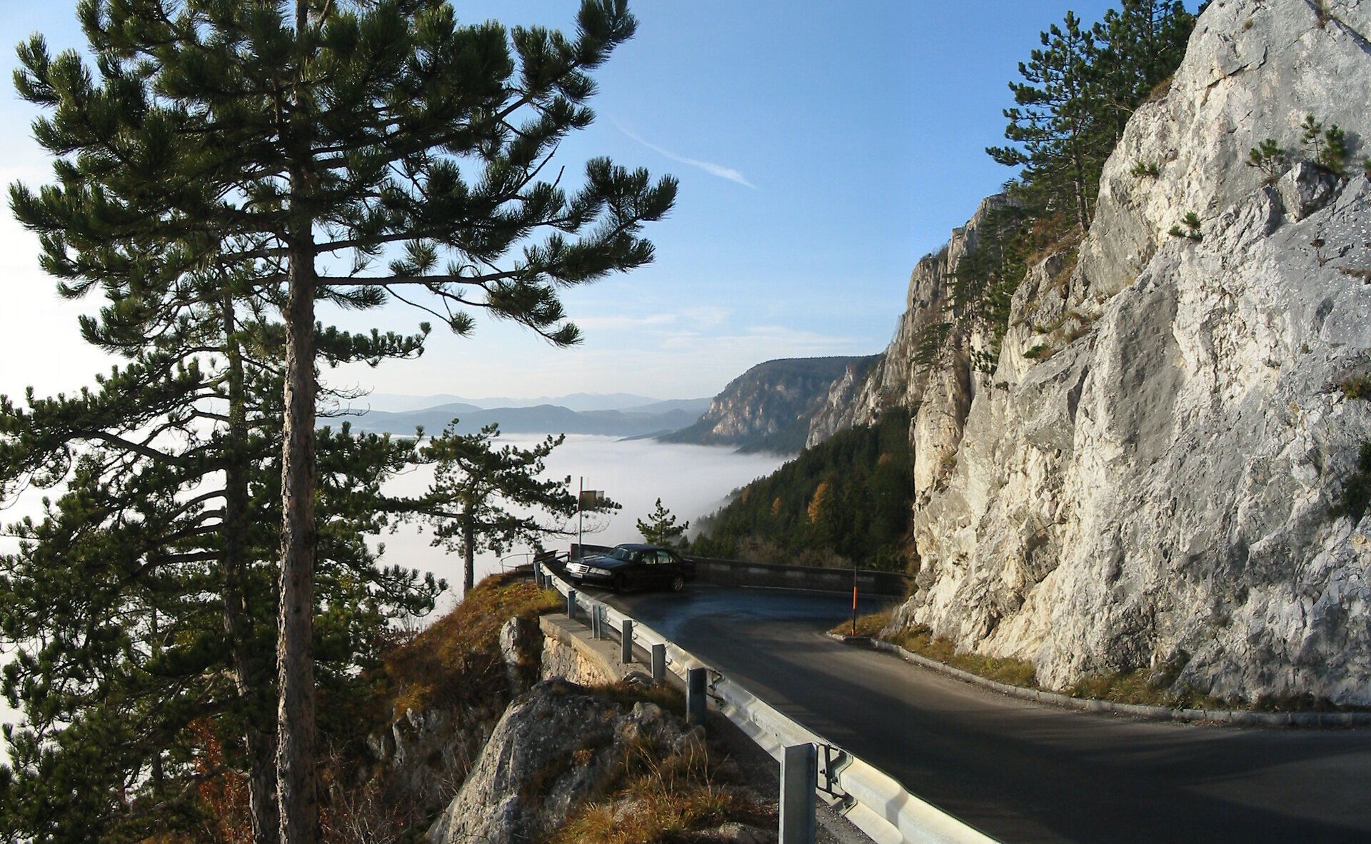 Eine kurvenreiche Straße schlängelt sich entlang majestätischer Felsen, während die Sonne sanft durch den Nebel blitzt. Die umgebenden Kiefern verleihen der Szenerie eine friedliche Atmosphäre, die zum Verweilen einlädt. Hier, wo die Natur ihre Schönheit entfaltet, wird jeder Moment zum unvergesslichen Erlebnis.