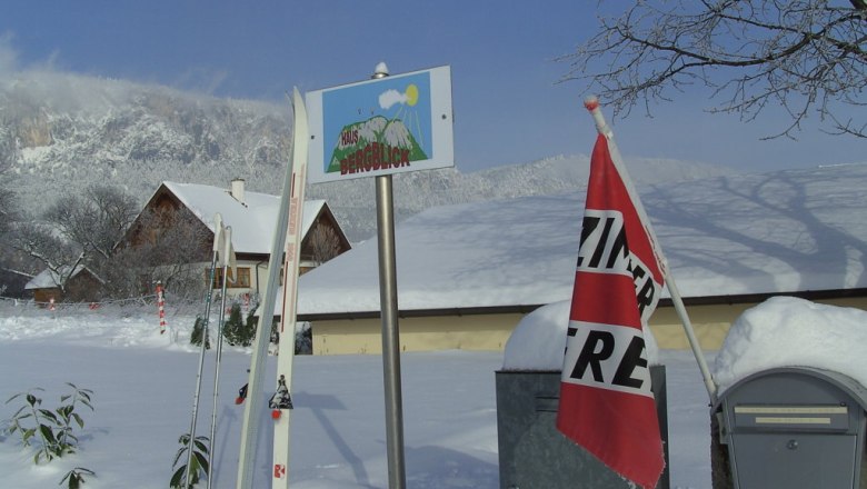 Winterlandschaft mit Skiern, einem Schild 'Haus Bergblick' und einer 'Zimmer frei'-Fahne.