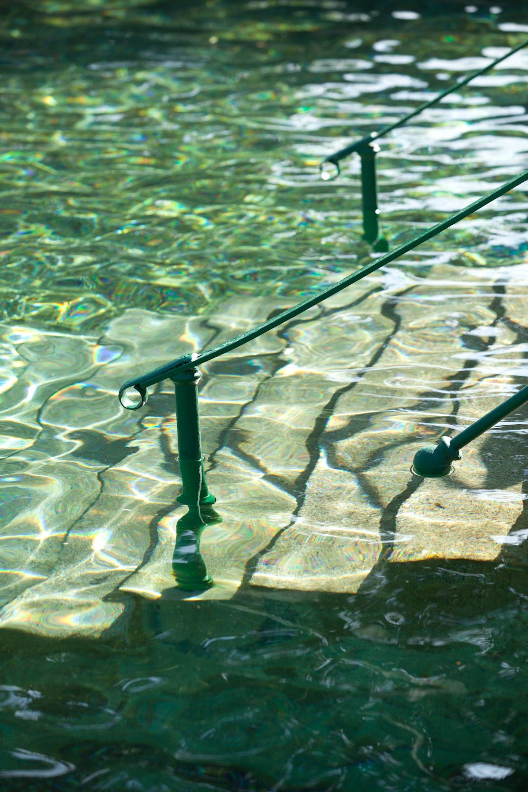 Nahaufnahme eines Geländers in einem Thermalbad mit klarem, grünlichem Wasser.