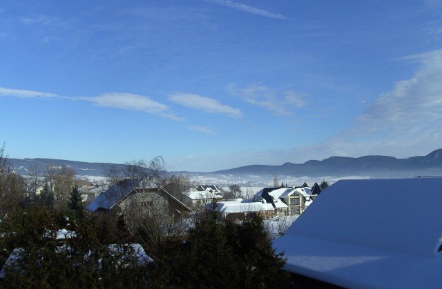 Winterlandschaft mit schneebedeckten D&auml;chern und Bergen im Hintergrund.