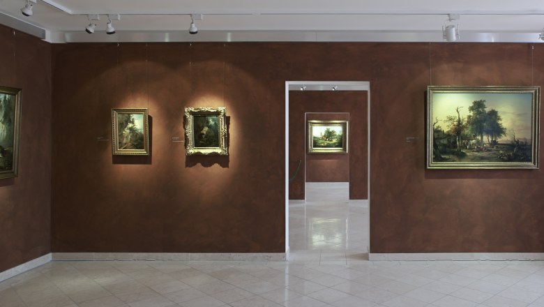 Innenansicht eines Museums mit Gemälden an braunen Wänden.