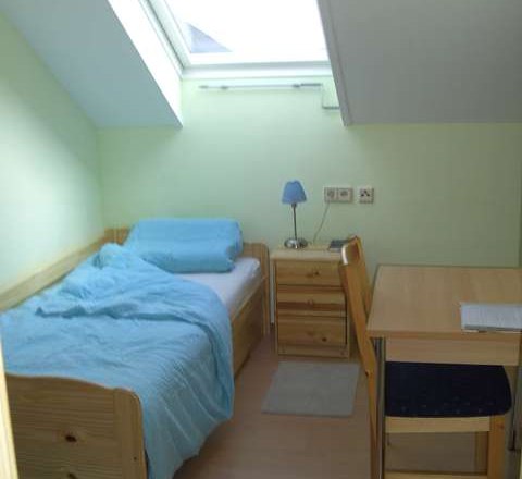 Ein kleines Einzelzimmer mit Bett, Schreibtisch und Dachfenster.