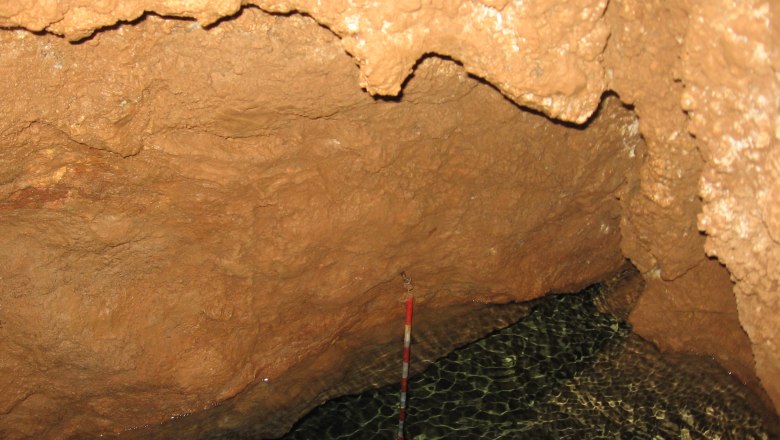 Interior view of a cave with water and brown rock walls.