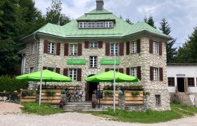 Steingeb&auml;ude mit gr&uuml;nem Dach und Sonnenschirmen vor dem Eingang.