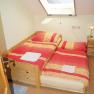A single room with a bed and an extra bed under a skylight. The beds are covered with red and yellow blankets.