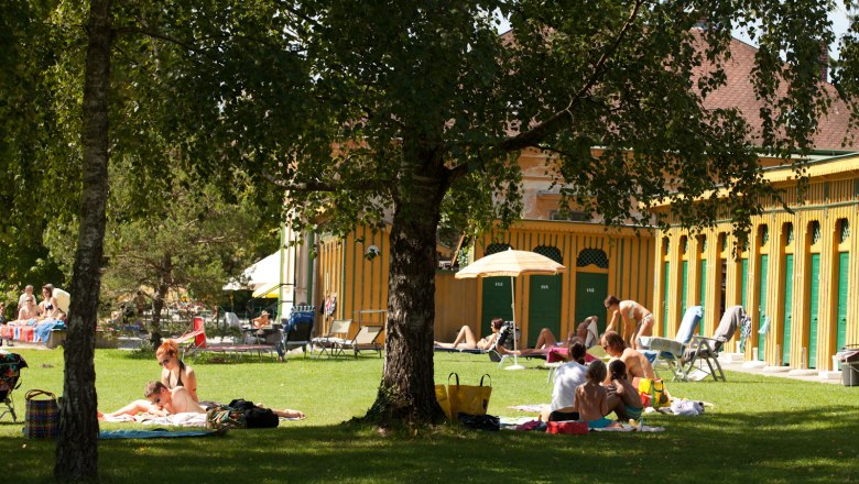 People relaxing on a lawn in front of a historic bathhouse.