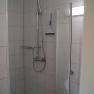 A tiled shower with shower head, shower fitting and squeegee on the wall.