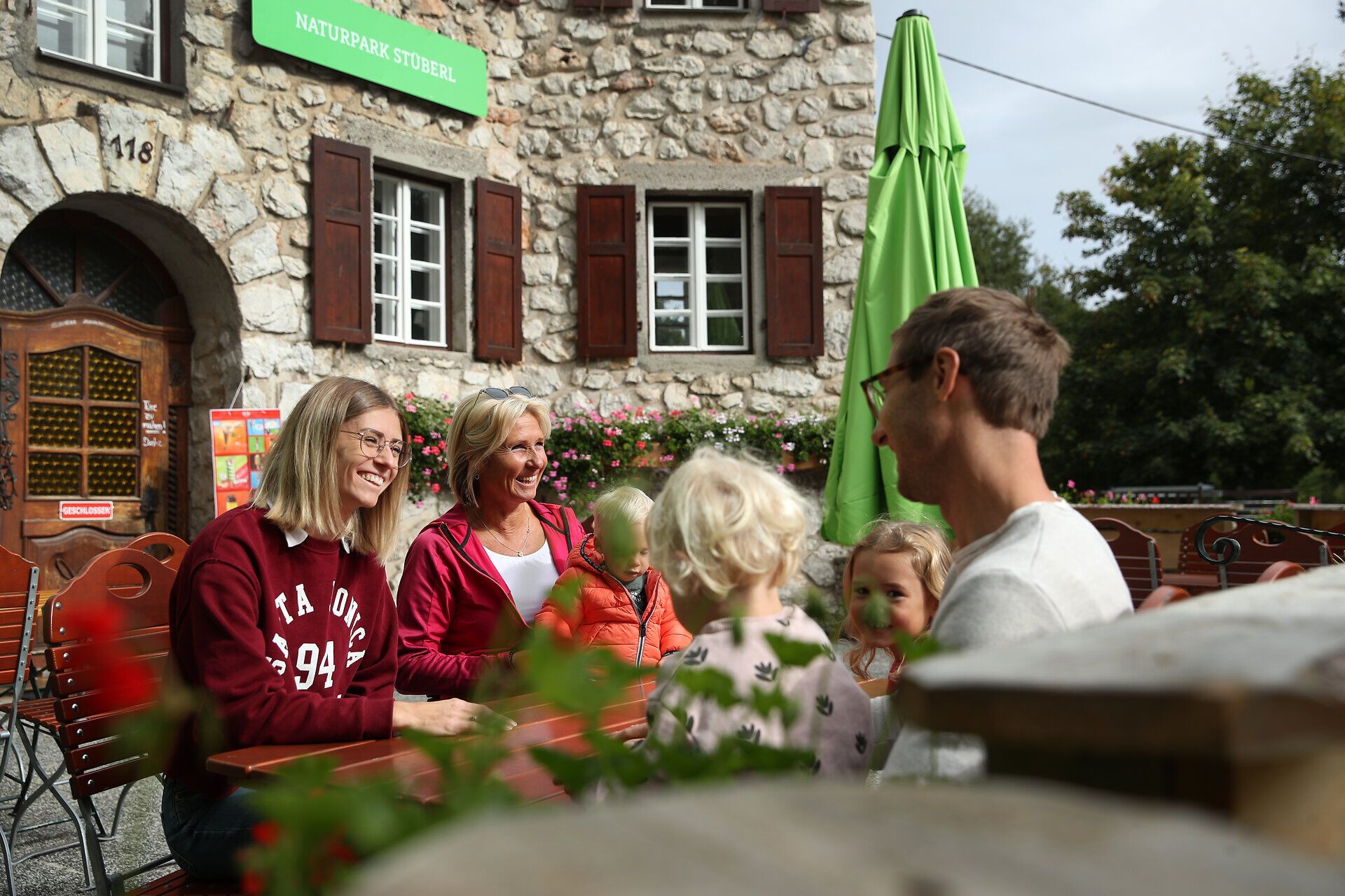 Familie und Freunde sitzen vor dem Naturpark Stüberl im Naturpark Hohe Wand an einem Tisch im Freien.
