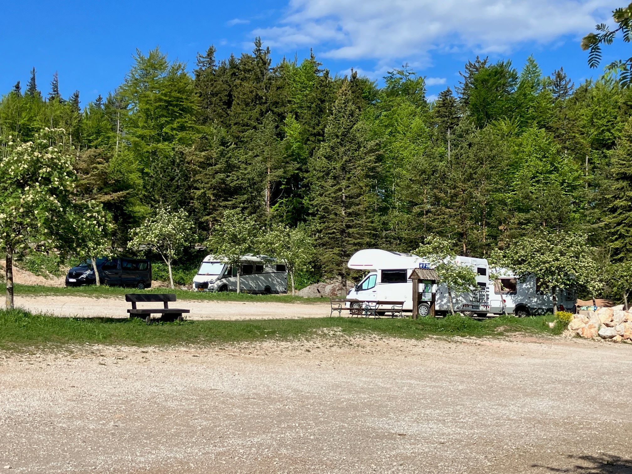 Motorhomes on a pitch in the countryside with trees and benches.