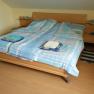 Double bed with blue bed linen in a room with wooden floor.