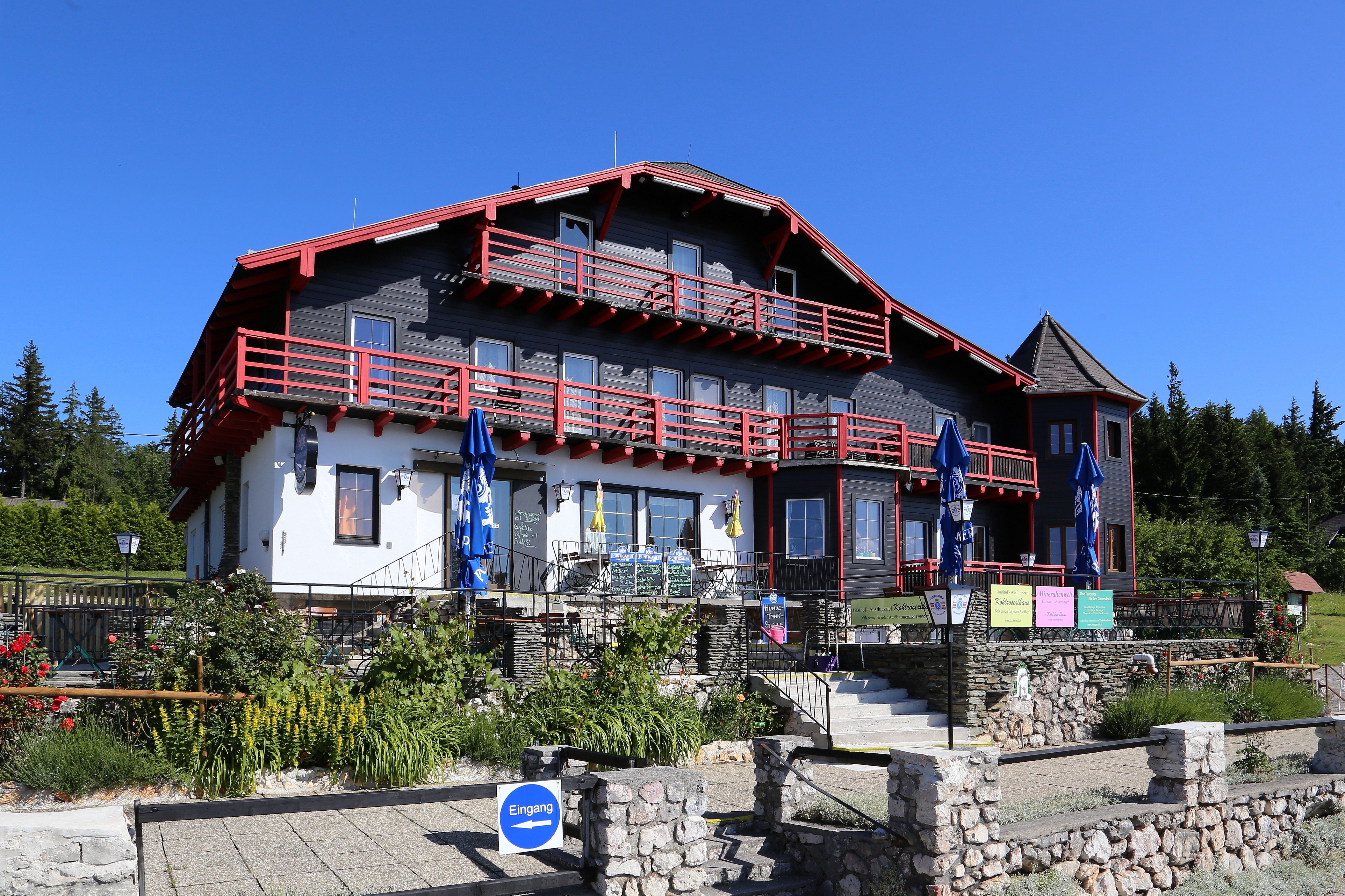 Ein großes, traditionelles Haus mit rotem Holz und weißen Wänden, umgeben von einem Garten und blauen Sonnenschirmen.