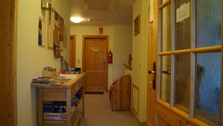 Ein Flur mit Holztüren, einem Tisch mit Broschüren und einer Pinnwand an der Wand.