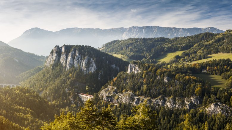 Panoramic view of the Semmering Railway in a mountainous landscape with forests and a viaduct.