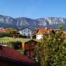 Blick auf ein Dorf mit Bergen im Hintergrund und blauen Himmel.