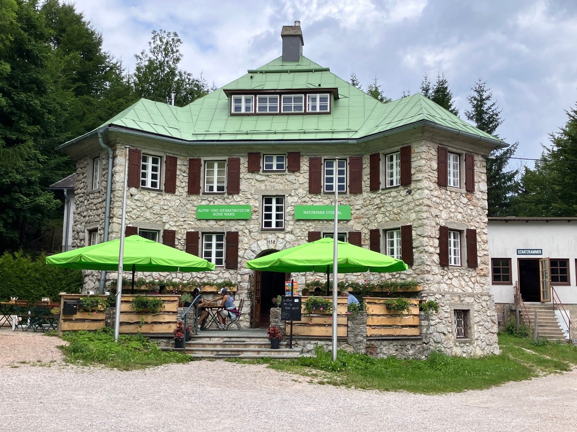 Stone building with a green roof and sunshades in front of the entrance.