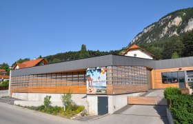 Modern building with wooden cladding and advertising sign for Mohr-Sederl Fruchtwelt, surrounded by green countryside and mountains.