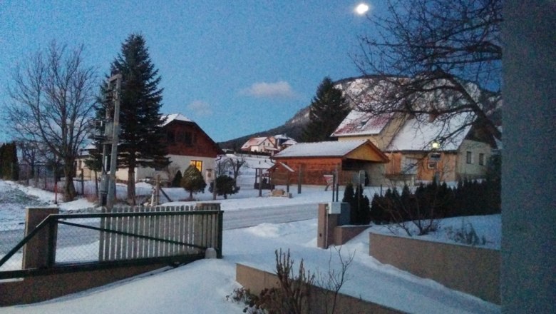 Winterliche Landschaft mit schneebedeckten H&auml;usern und B&auml;umen bei D&auml;mmerung.