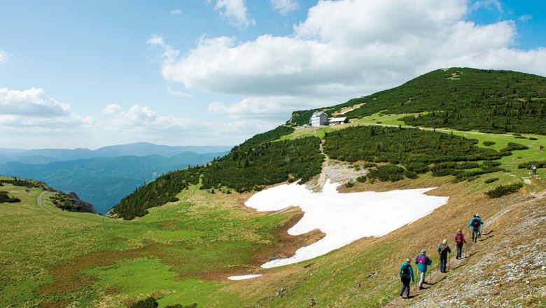 Wanderer auf der Raxalpe mit Schnee und Bergh&uuml;tte im Hintergrund.