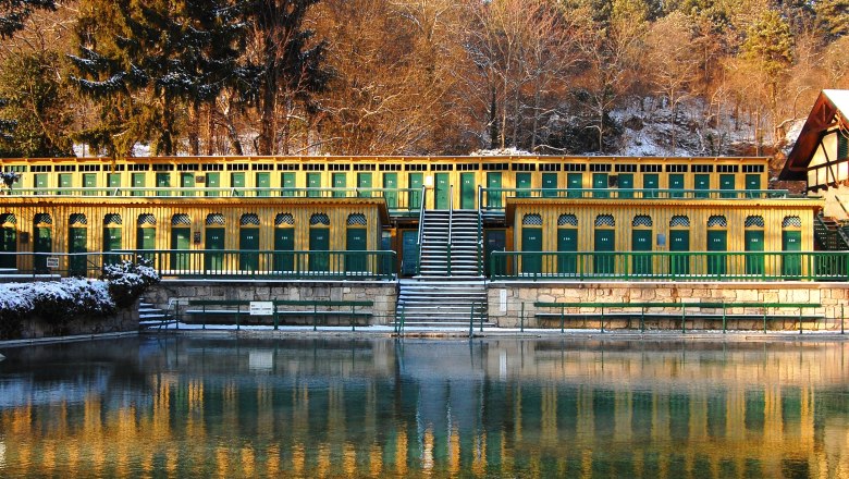 Historisches Thermalbad mit gelben und gr&uuml;nen Kabinen, umgeben von B&auml;umen im Winter.