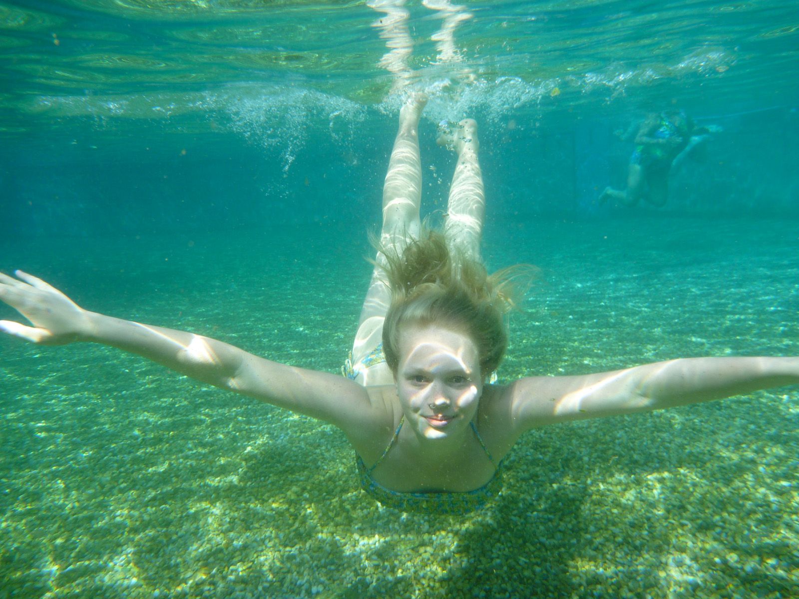 Unterwasseraufnahme eines Mädchens, das in einem klaren Naturbecken schwimmt.