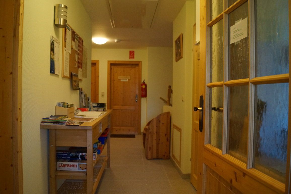 Egy előszoba faajtókkal, egy asztal prospektusokkal és játékokkal, és egy pinboard a falon.