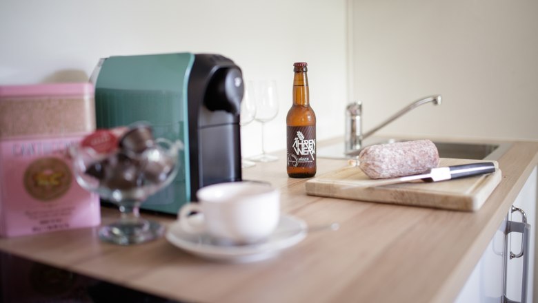 K&uuml;chenarbeitsplatte mit Kaffeemaschine, Bierflasche, Salami und Messer.