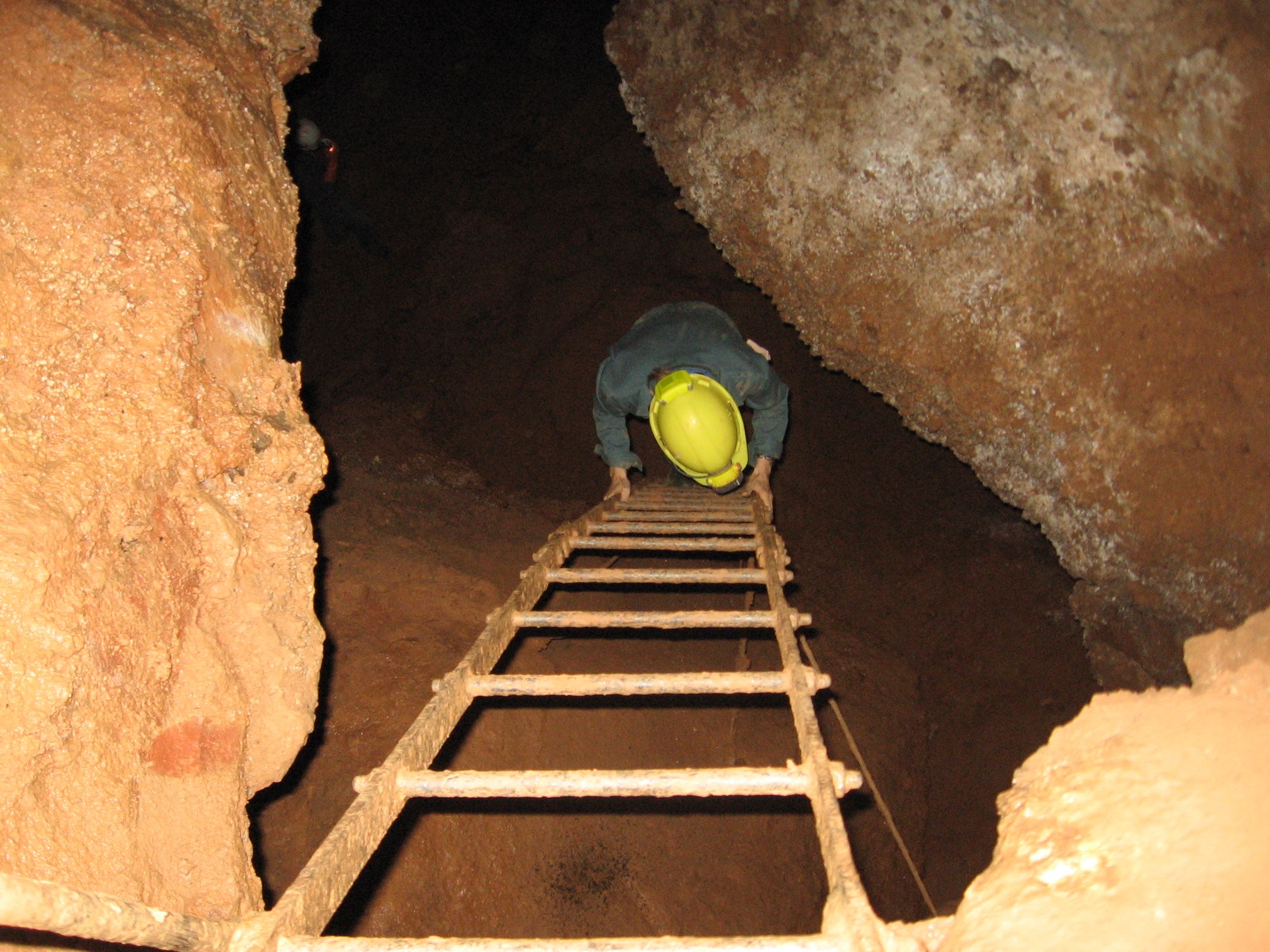 Person wearing a helmet climbs down a ladder in a cave.
