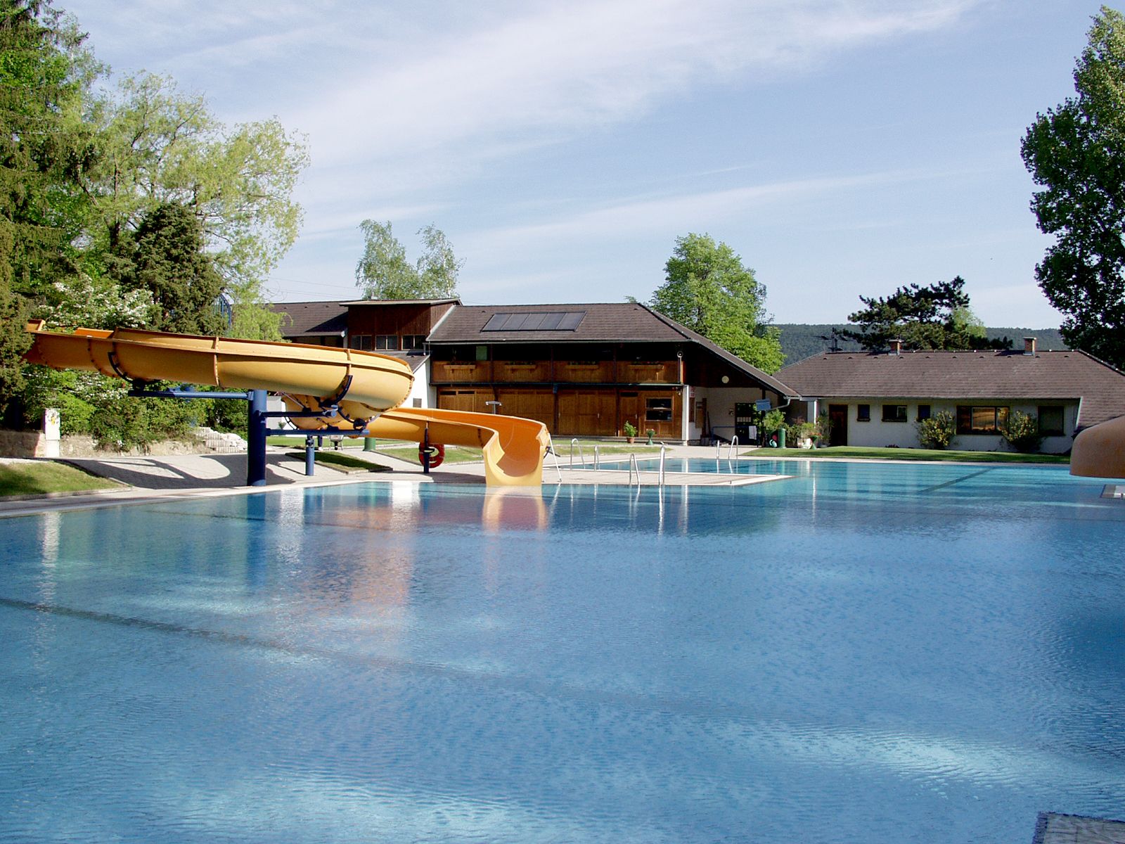 Ein Freibad mit Rutsche und Gebäuden im Hintergrund.