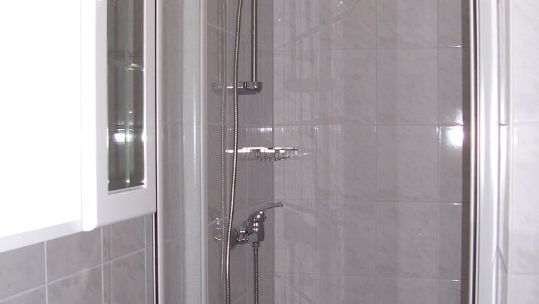 A modern shower cubicle with glass doors and chrome shower head in a tiled bathroom.