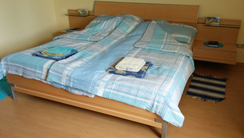 Double bed with blue bed linen in a room with wooden floor.