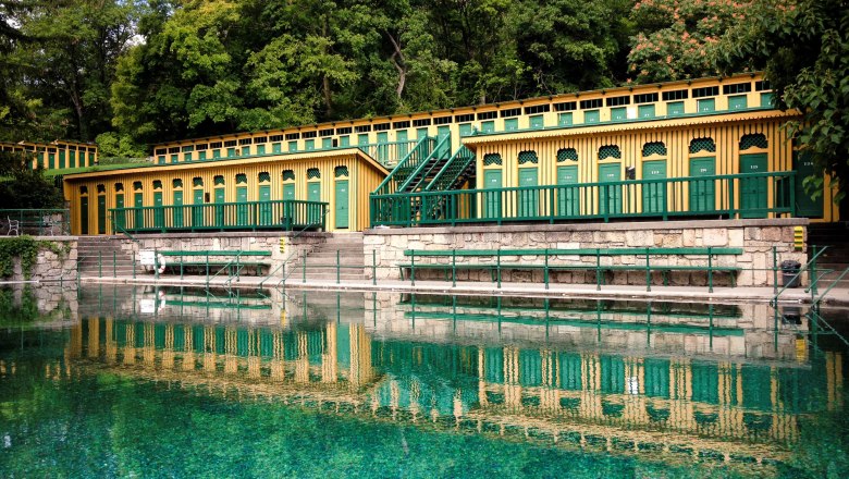 Historisches Badehaus in Bad Fischau mit grün-gelber Fassade und reflektierendem Wasser.