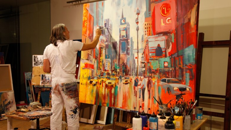 Ein K&uuml;nstler malt ein lebhaftes Stadtbild auf einer gro&szlig;en Leinwand in einem Atelier.