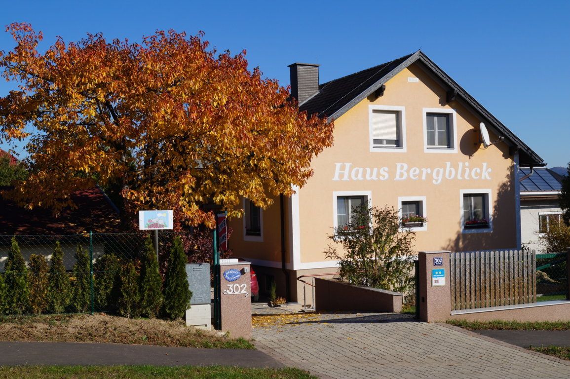 Egy sárga ház "Haus Bergblick" felirattal és egy őszi fával előtte.
