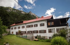 Ein gro&szlig;es Geb&auml;ude mit rotem Dach vor einem bewaldeten Berghang.