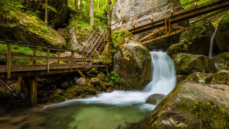Waterfall with wooden bridges and steps in a wooded area.