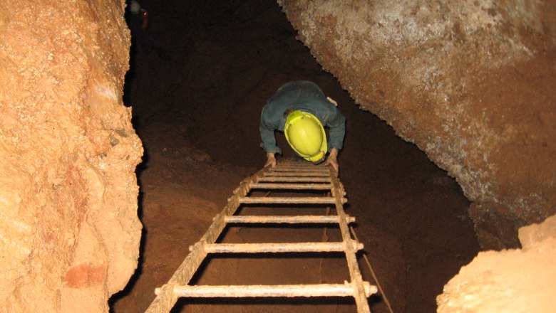 Person wearing a helmet climbs down a ladder in a cave.