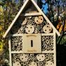 Ein Bienenhotel aus Holz mit verschiedenen Röhren und Löchern, montiert an einem Pfosten im Freien.