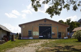 Außenansicht des Dorfmuseums Maiersdorf mit Holzhäusern und Bäumen.